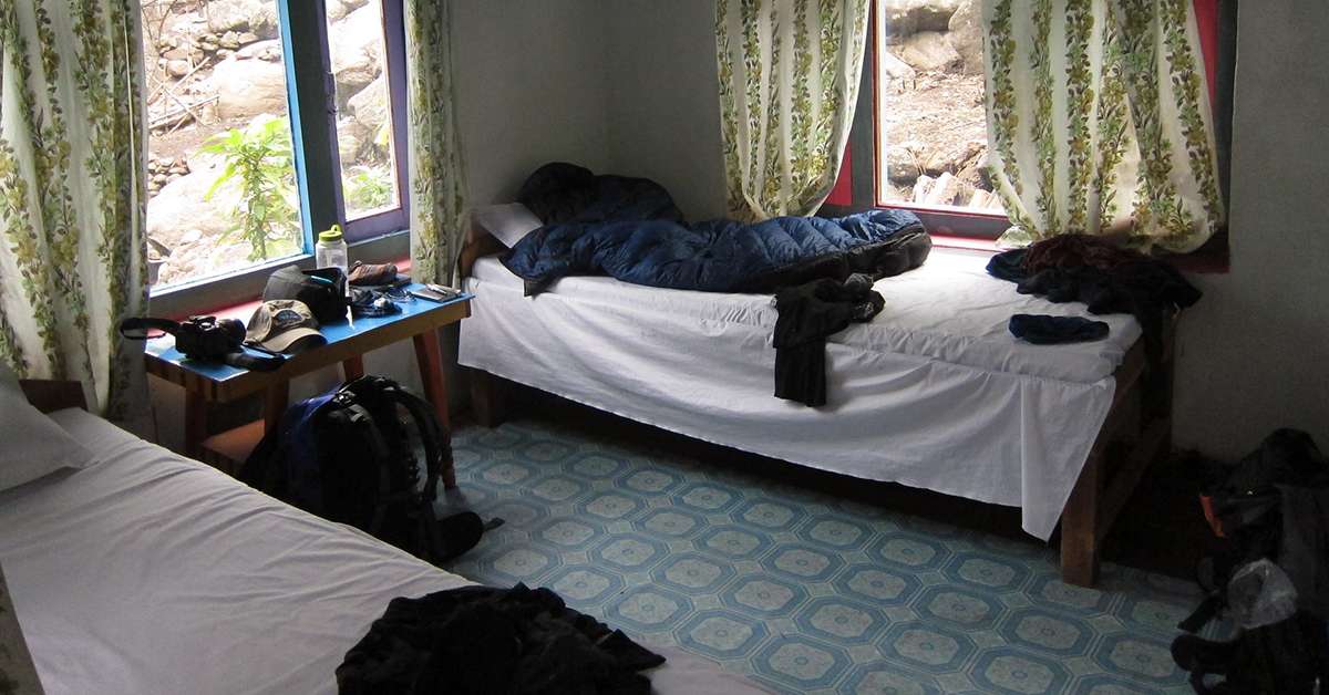 Simple guesthouse room with mattress, blankets, and shared bathroom on the Manaslu Circuit Trek.