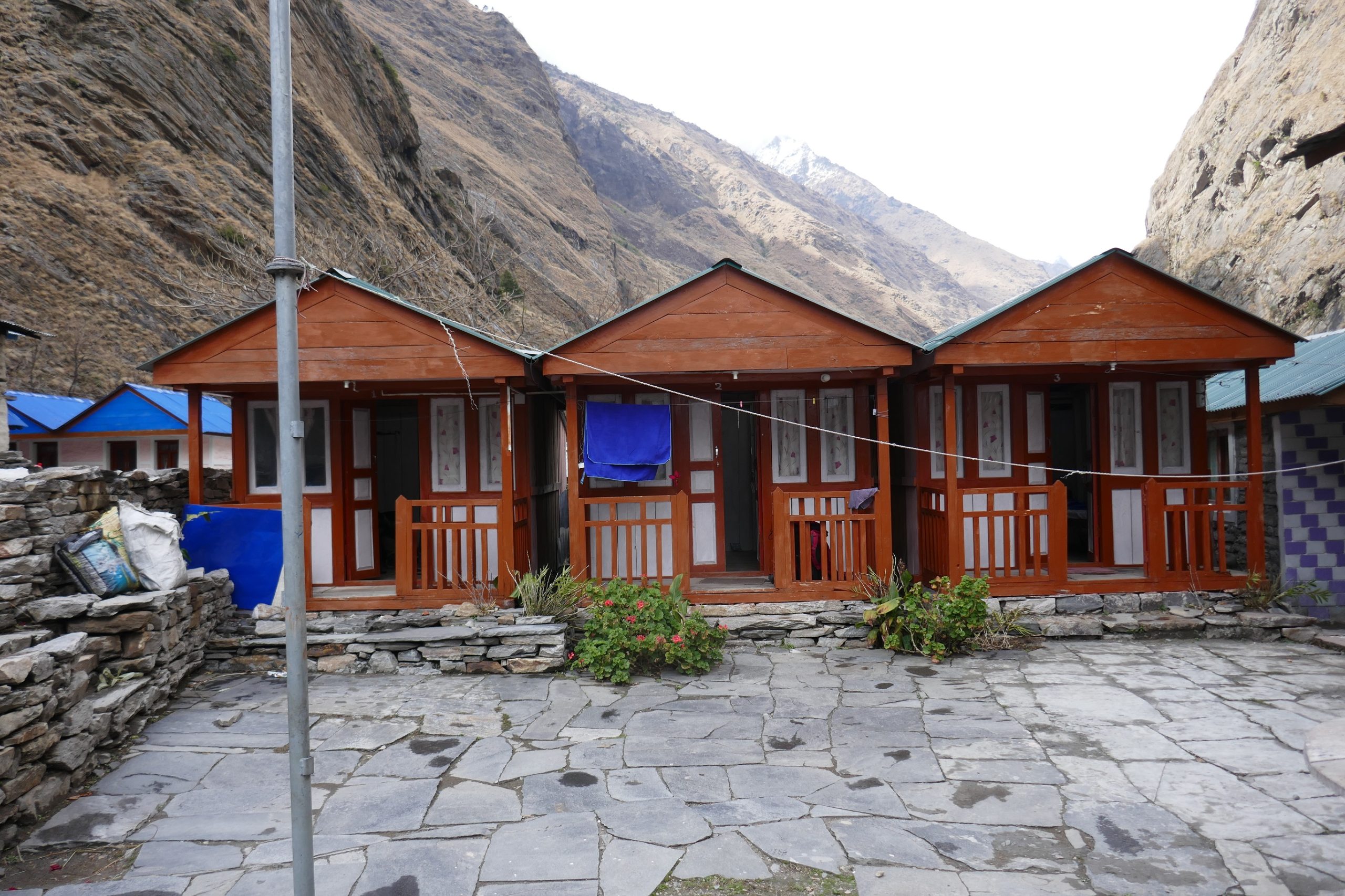 Traditional tea house in the Manaslu region with stone walls and tin roof, surrounded by mountains and offering shelter for trekkers.